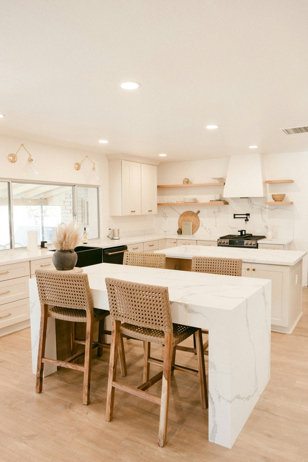 Kitchen with white marble islands, woven bar stools and light wood floors